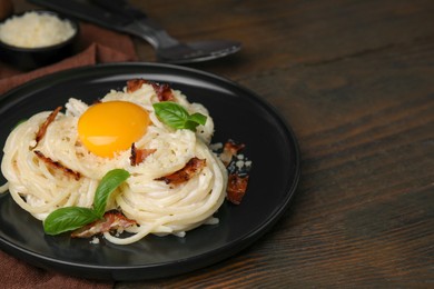 Photo of Delicious pasta Carbonara with egg yolk, bacon and basil on wooden table, closeup