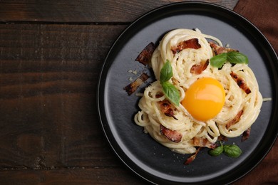 Photo of Delicious pasta Carbonara with egg yolk, bacon and basil on wooden table, top view. Space for text