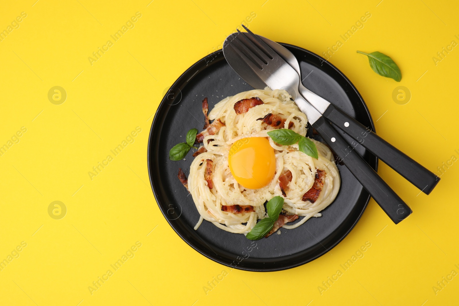 Photo of Delicious pasta Carbonara served on yellow table, top view. Space for text