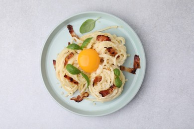 Photo of Delicious pasta Carbonara with egg yolk, bacon and basil on light gray table, top view