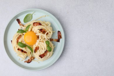 Delicious pasta Carbonara with egg yolk, bacon and basil on light gray table, top view. Space for text