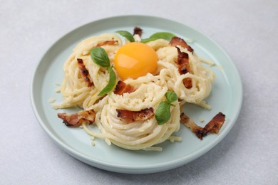 Photo of Delicious pasta Carbonara with egg yolk, bacon and basil on light gray table, closeup