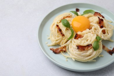 Photo of Delicious pasta Carbonara with egg yolk, bacon and basil on light gray table, closeup. Space for text