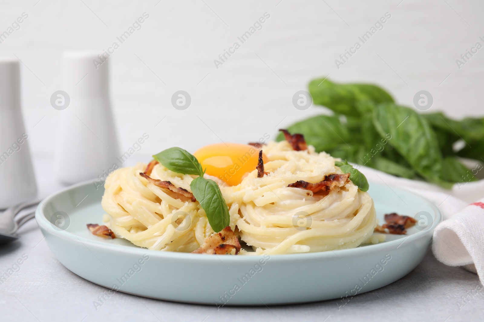 Photo of Delicious pasta Carbonara with egg yolk, bacon and basil on light gray table, closeup