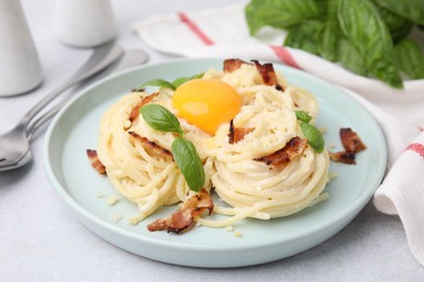 Photo of Delicious pasta Carbonara with egg yolk, bacon and basil on light gray table, closeup