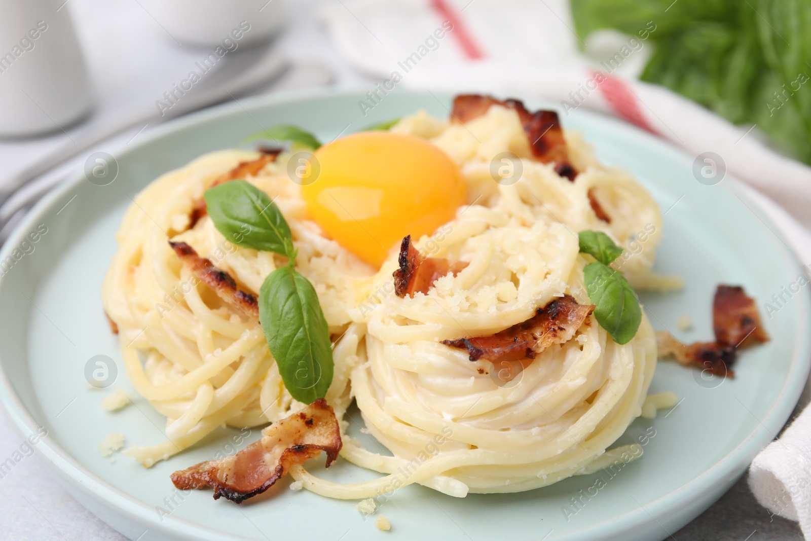 Photo of Delicious pasta Carbonara with egg yolk, bacon and basil on table, closeup