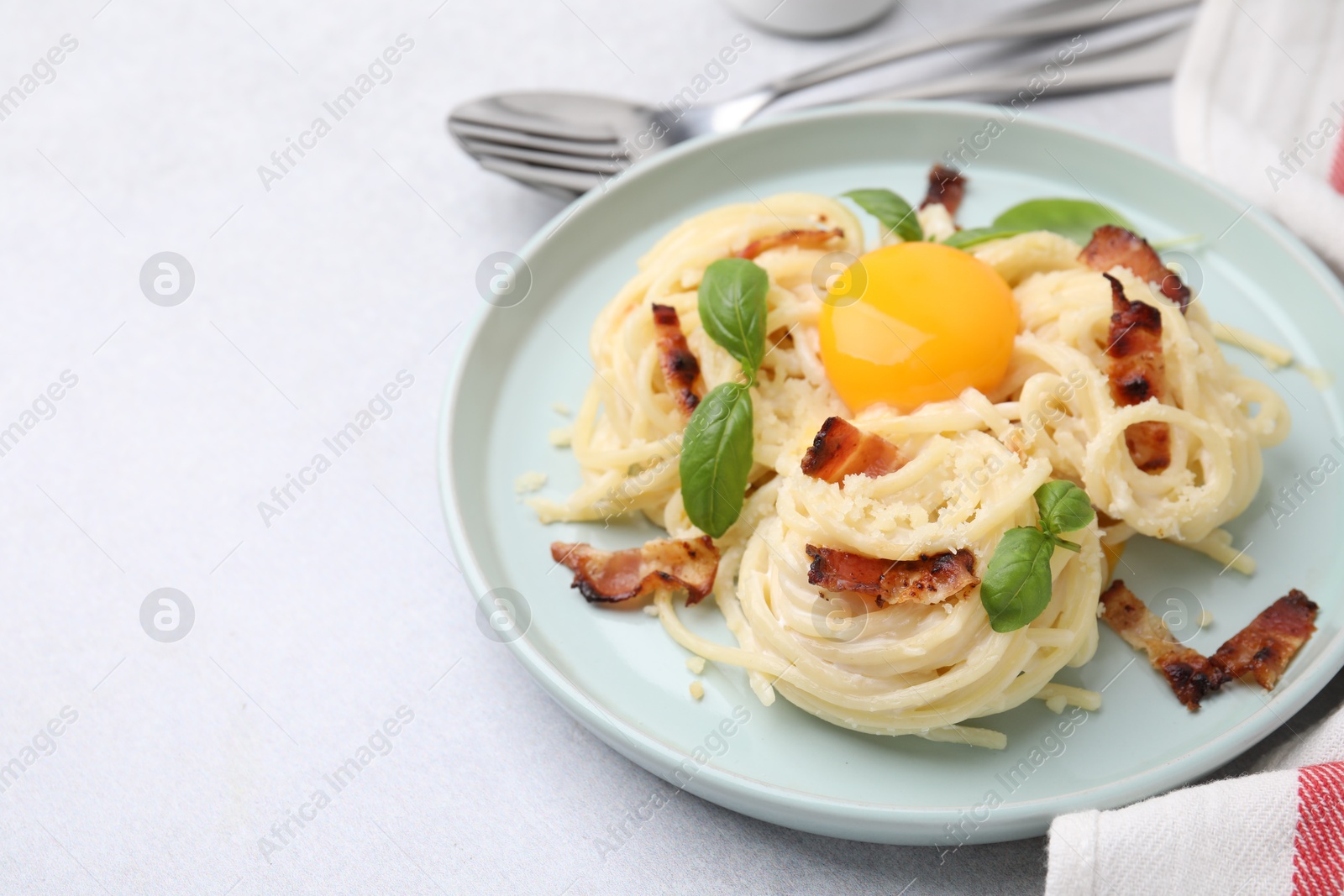 Photo of Delicious pasta Carbonara with egg yolk, bacon and basil on light gray table, closeup. Space for text