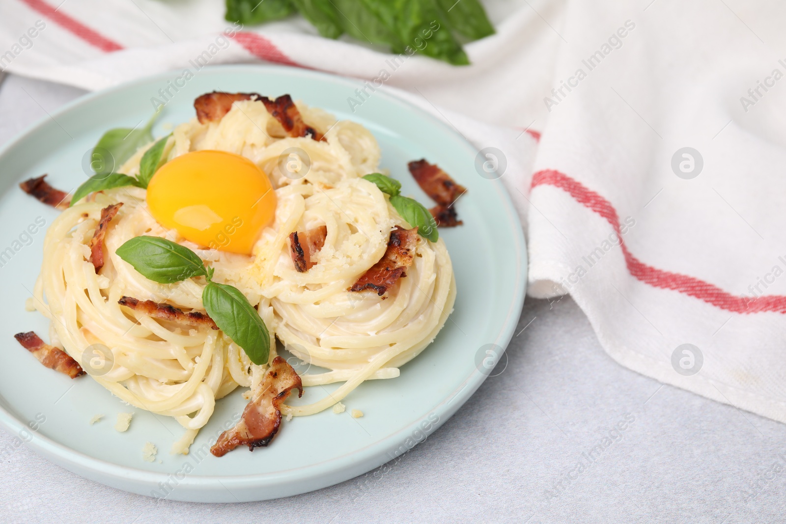 Photo of Delicious pasta Carbonara with egg yolk, bacon and basil on light gray table, closeup