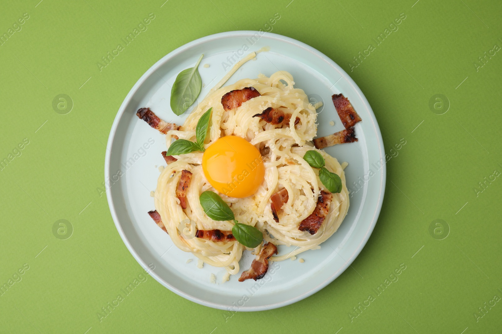 Photo of Delicious pasta Carbonara with egg yolk, bacon and basil on green table, top view