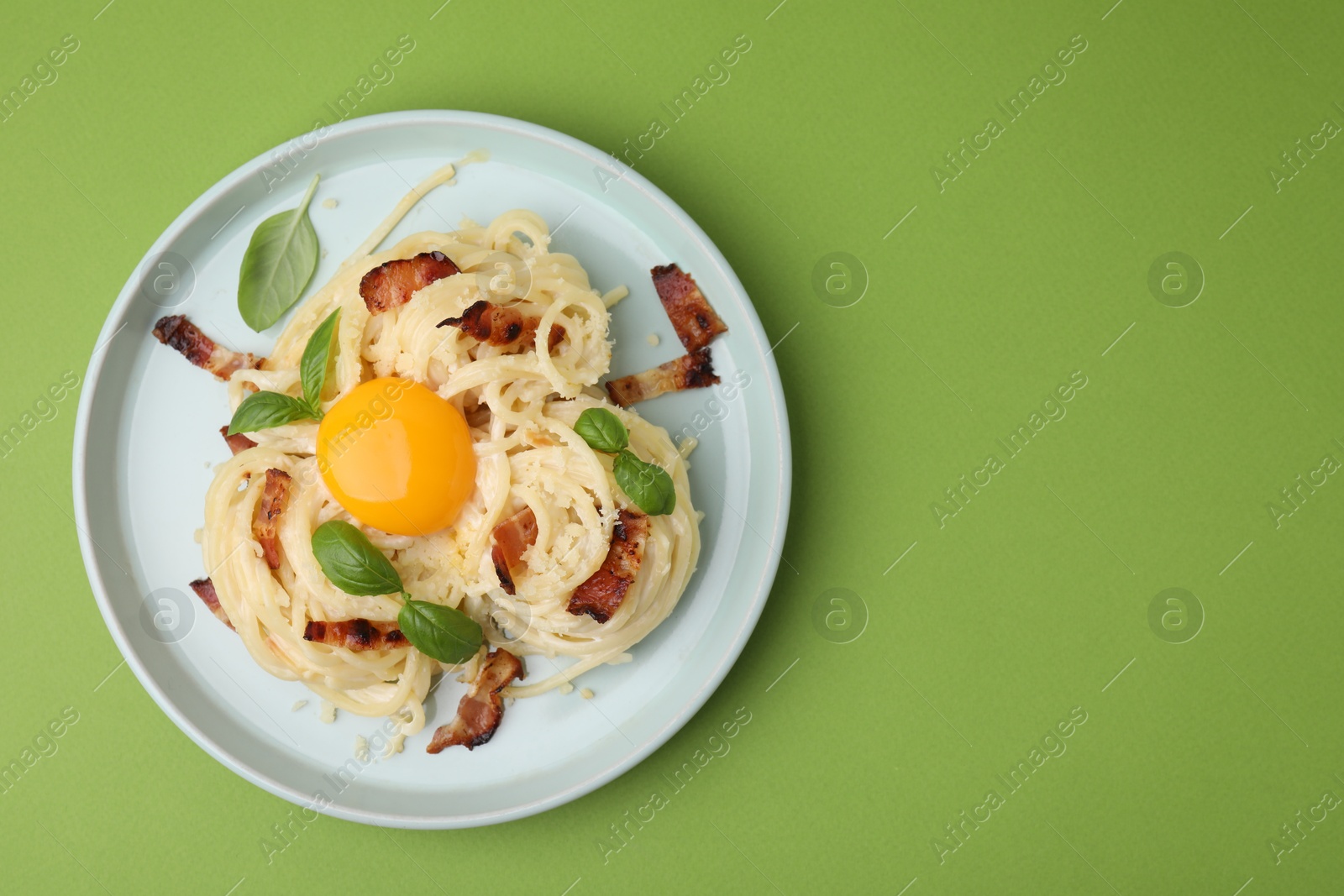 Photo of Delicious pasta Carbonara with egg yolk, bacon and basil on green table, top view. Space for text