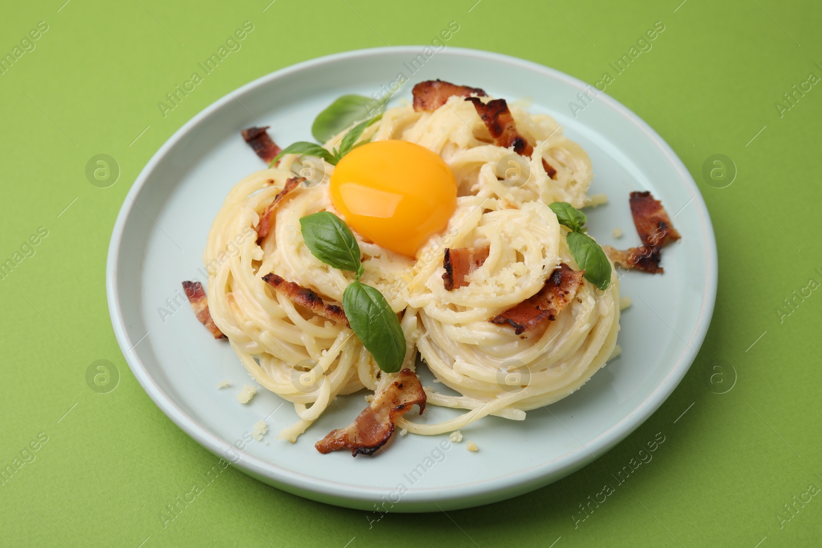 Photo of Delicious pasta Carbonara with egg yolk, bacon and basil on green table, closeup