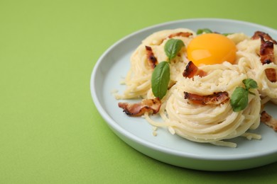 Photo of Delicious pasta Carbonara with egg yolk, bacon and basil on green table, closeup. Space for text