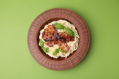 Photo of Delicious pasta Carbonara with bacon and basil on green table, top view