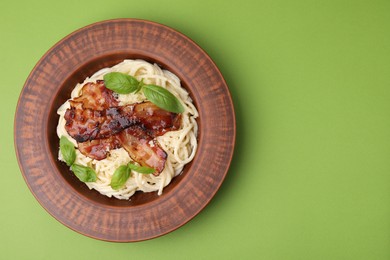 Delicious pasta Carbonara with bacon and basil on green table, top view. Space for text