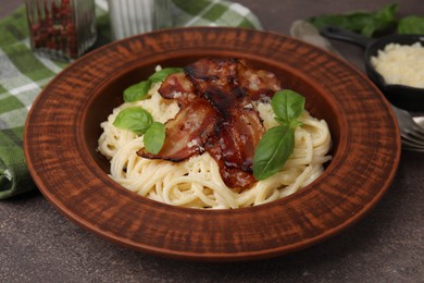 Delicious pasta Carbonara with bacon and basil on brown table, closeup