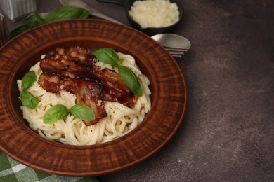 Photo of Delicious pasta Carbonara with bacon and basil on brown table, closeup. Space for text