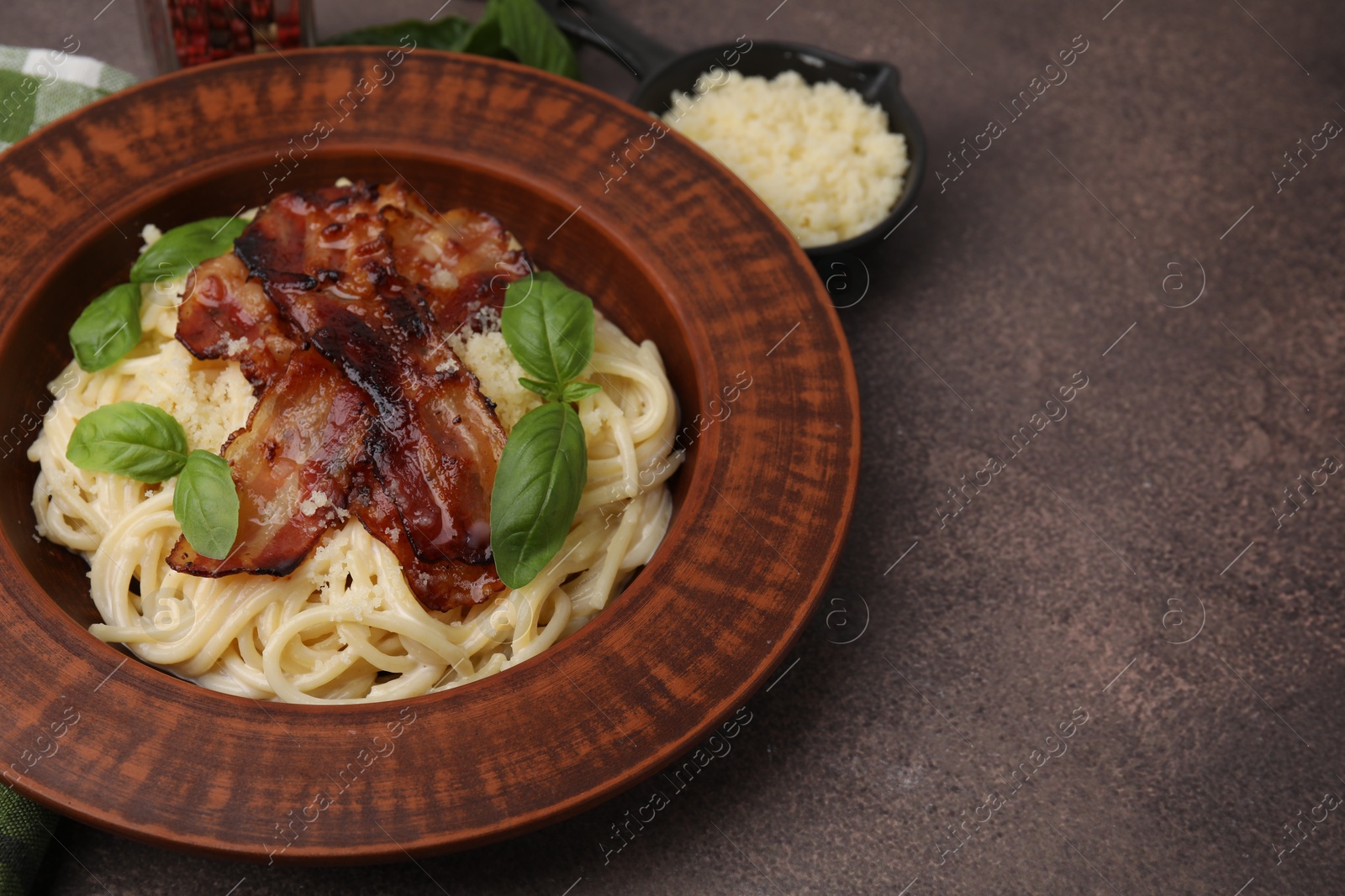 Photo of Delicious pasta Carbonara with bacon and basil on brown table, closeup. Space for text