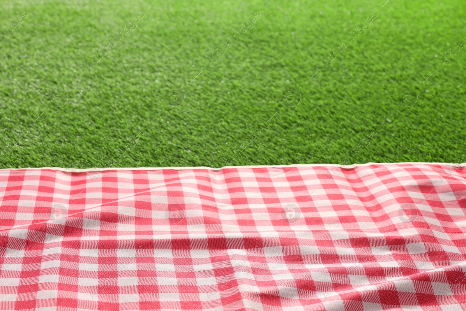 Photo of Checkered picnic tablecloth on green grass, closeup. Space for text