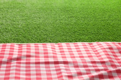 Checkered picnic tablecloth on green grass, closeup. Space for text