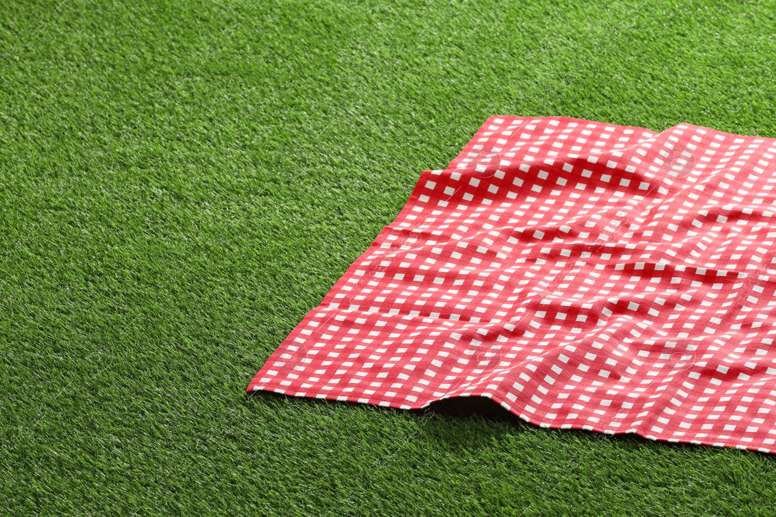 Photo of Checkered picnic tablecloth on green grass, closeup. Space for text