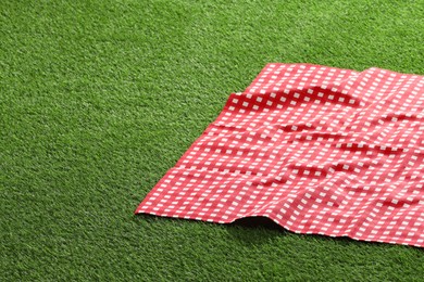 Photo of Checkered picnic tablecloth on green grass, closeup. Space for text