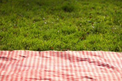 Photo of Checkered picnic tablecloth on green grass, closeup. Space for text