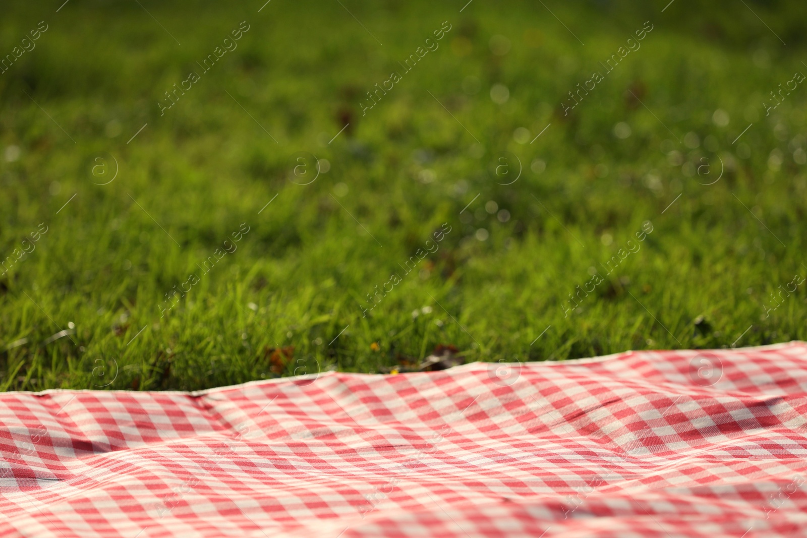 Photo of Checkered picnic tablecloth on green grass, closeup. Space for text