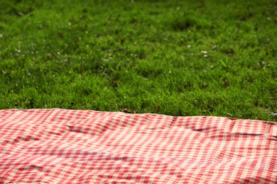 Photo of Checkered picnic tablecloth on green grass, closeup. Space for text