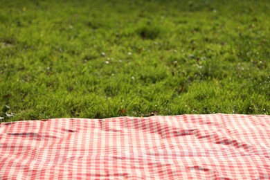 Photo of Checkered picnic tablecloth on green grass, closeup. Space for text