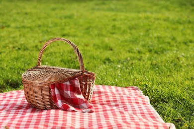 Photo of One picnic wicker basket with checkered napkin and blanket on green grass. Space for text