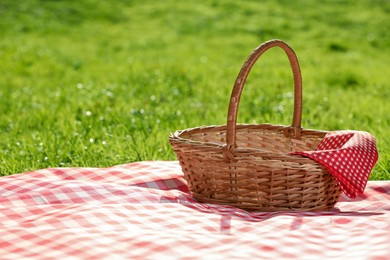 Photo of One picnic wicker basket with checkered napkin and blanket on green grass. Space for text