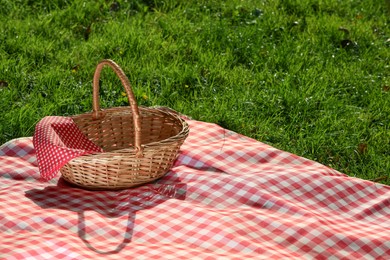 Photo of One picnic wicker basket with checkered napkin and blanket on green grass. Space for text