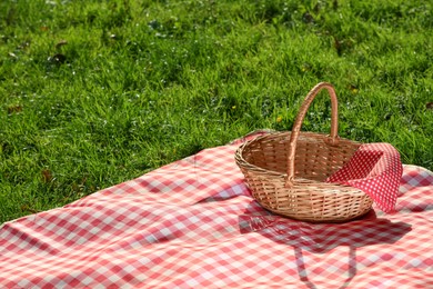 Photo of One picnic wicker basket with checkered napkin and blanket on green grass. Space for text