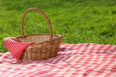 Photo of One picnic wicker basket with checkered napkin and blanket on green grass. Space for text