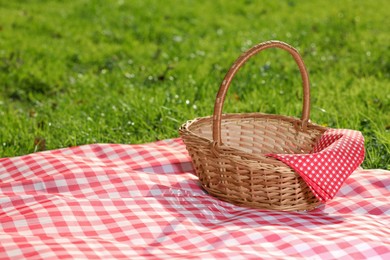 Photo of One picnic wicker basket with checkered napkin and blanket on green grass. Space for text