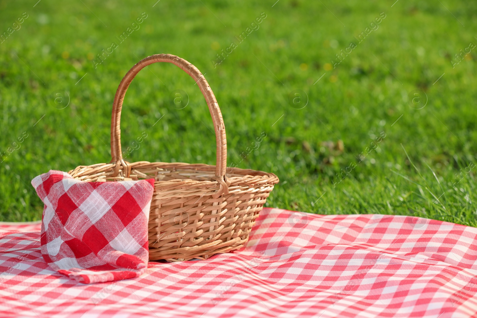 Photo of One picnic wicker basket with checkered napkin and blanket on green grass. Space for text