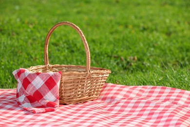 Photo of One picnic wicker basket with checkered napkin and blanket on green grass. Space for text