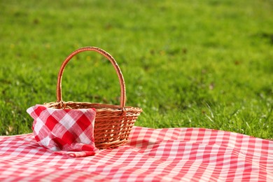 Photo of One picnic wicker basket with checkered napkin and blanket on green grass. Space for text