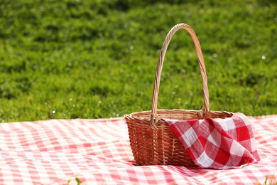 Photo of One picnic wicker basket with checkered napkin and blanket on green grass. Space for text