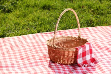 Photo of One picnic wicker basket with checkered napkin and blanket on green grass. Space for text