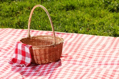 Photo of One picnic wicker basket with checkered napkin and blanket on green grass. Space for text