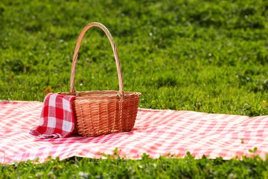 Photo of One picnic wicker basket with checkered napkin and blanket on green grass. Space for text