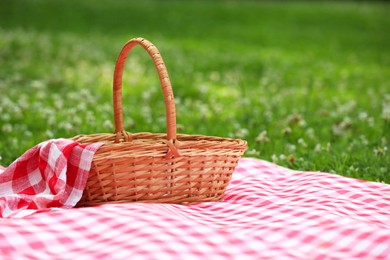 Photo of One picnic wicker basket with checkered napkin and blanket on green grass. Space for text