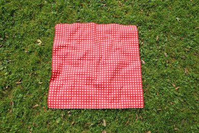 Photo of One checkered picnic tablecloth on green grass, above view