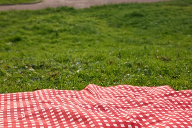 Photo of Checkered picnic tablecloth on green grass, closeup. Space for text