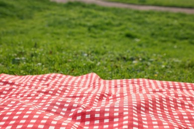 Photo of Checkered picnic tablecloth on green grass, closeup. Space for text