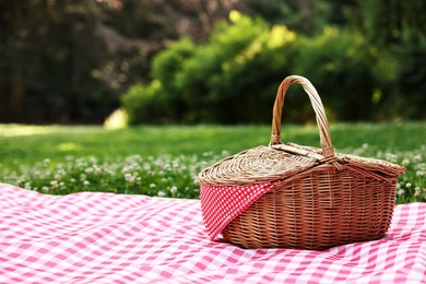 Photo of One picnic wicker basket with checkered napkin and blanket on green grass. Space for text