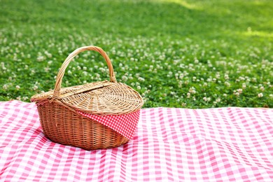 Photo of One picnic wicker basket with checkered napkin and blanket on green grass. Space for text