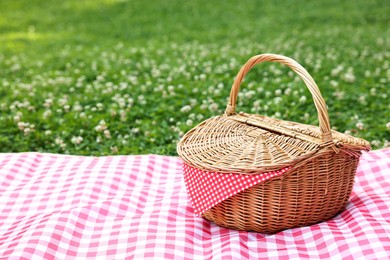 Photo of One picnic wicker basket with checkered napkin and blanket on green grass. Space for text