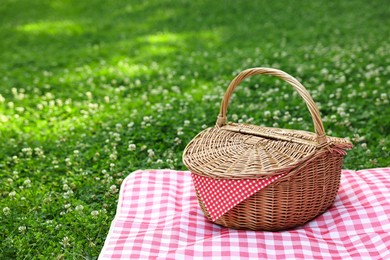 Photo of One picnic wicker basket with checkered napkin and blanket on green grass. Space for text